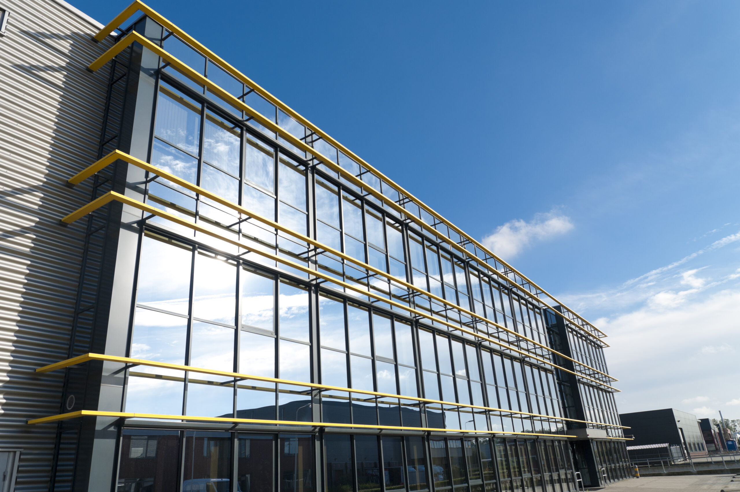 A sleek, modern commercial building with large reflective glass windows and yellow accents, under a clear blue sky.